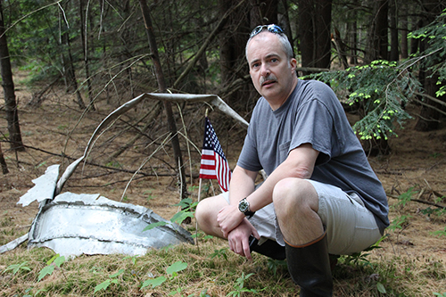 With the help of Pat Cutter and the permission of Roy Sell, Peter Ferraro planted an American flag at the site of the crash of an Air Force plane that crashed in Andover in 1959, killing all aboard. Peter is shown here at the crash site with the flag and some of the wreckage. Photo: Marc Goldstein
